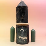 The Celestial Catskills 12oz Soy Candle in front of a large crystal tower and surrounded by two smaller crystals all on a pink and yellow background.