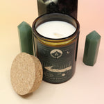 The Celestial Catskills 12oz Soy Candle in front of a large crystal tower and surrounded by two smaller crystals all on a pink and yellow background.