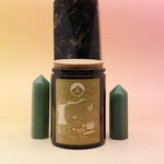 The Golden Days 12oz Soy Candle in front of a large crystal tower surrounded by two smaller crystal towers all on a pink and yellow background.