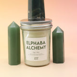 The Fog & Fern Soy Candle surrounded by green crystal tower all on a pink and yellow background.