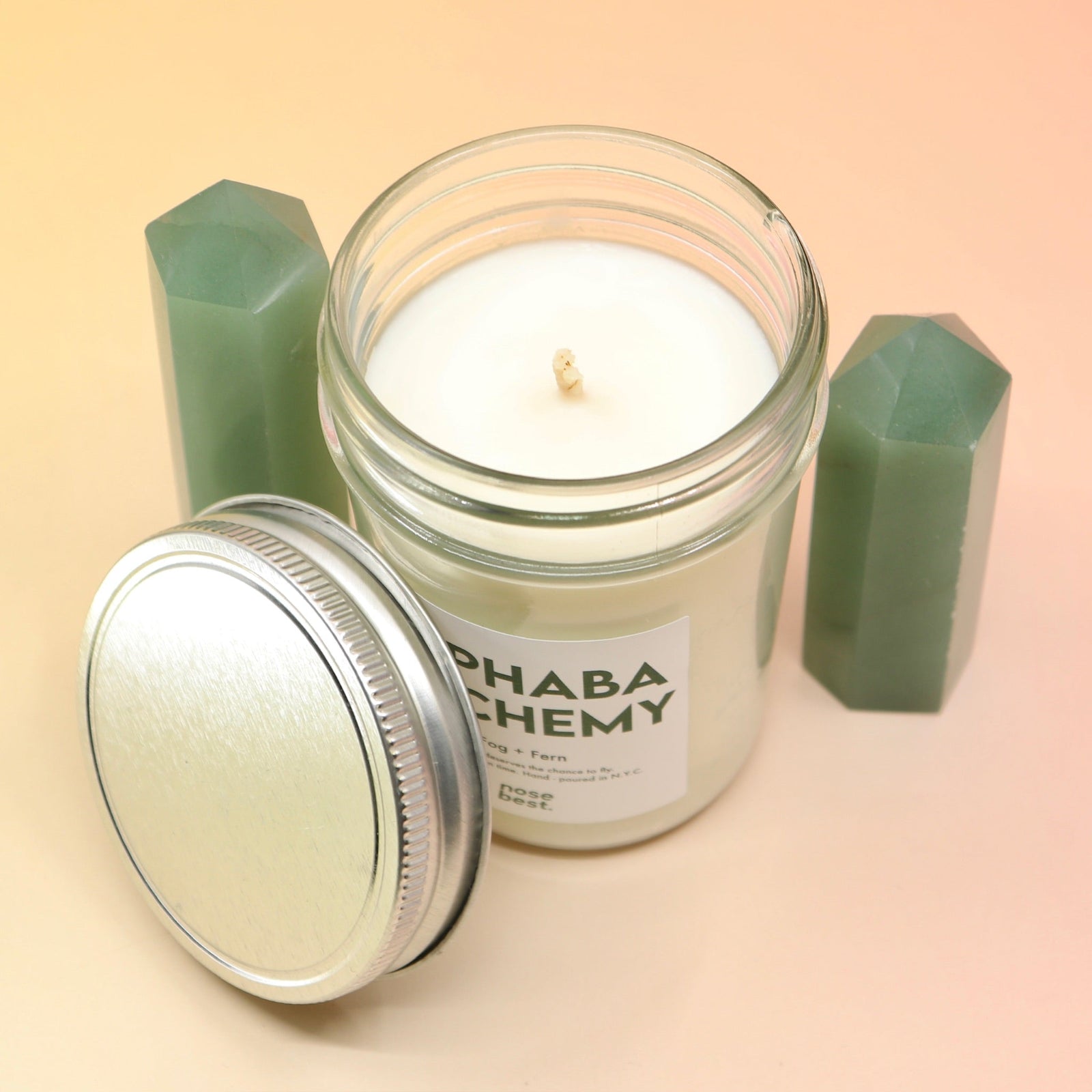 The Fog & Fern Soy Candle surrounded by green crystal tower all on a pink and yellow background.