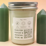 The Fog & Fern Soy Candle surrounded by green crystal tower all on a pink and yellow background.