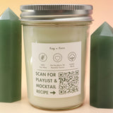 The Fog & Fern Soy Candle surrounded by green crystal tower all on a pink and yellow background.