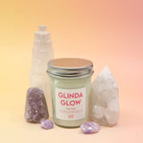 The Bubblegum Pop Glinda Soy Candle surrounded by various crystals all on a pink and yellow background.