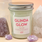 The Bubblegum Pop Glinda Soy Candle surrounded by various crystals all on a pink and yellow background.