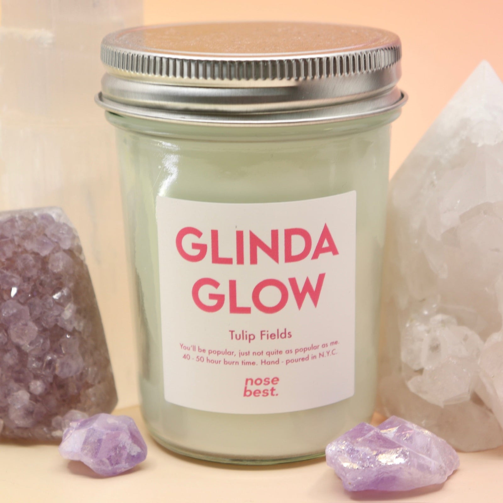 The Bubblegum Pop Glinda Soy Candle surrounded by various crystals all on a pink and yellow background.
