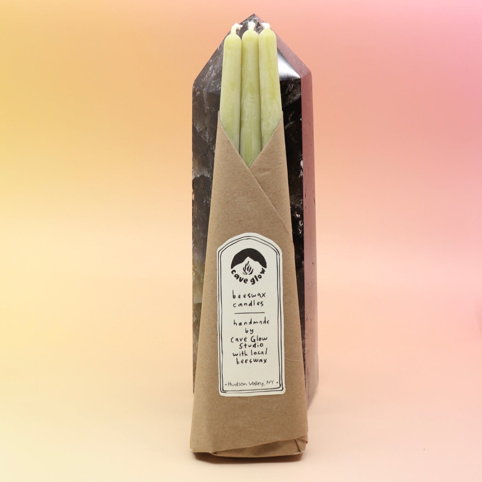 The straight Chartreuse Beeswax Taper Candles against a crystal tower all on a pink and yellow background.