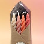 An up-close image of the Gathering Beeswax Spiral Taper Candles against a crystal tower all on a pink and yellow background.