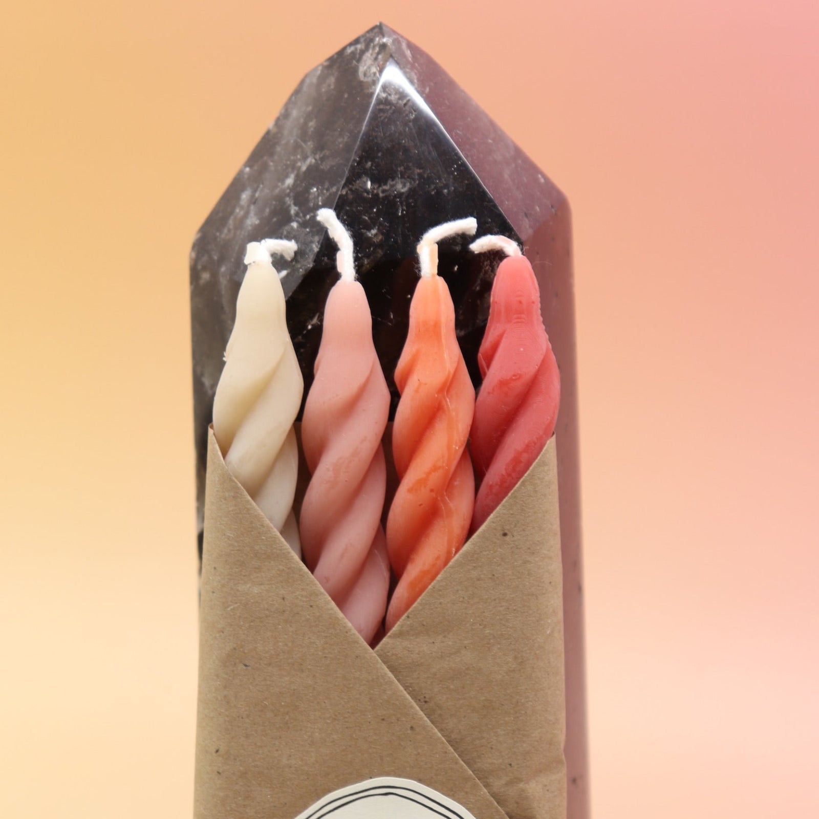 An up-close image of the Gathering Beeswax Spiral Taper Candles against a crystal tower all on a pink and yellow background.