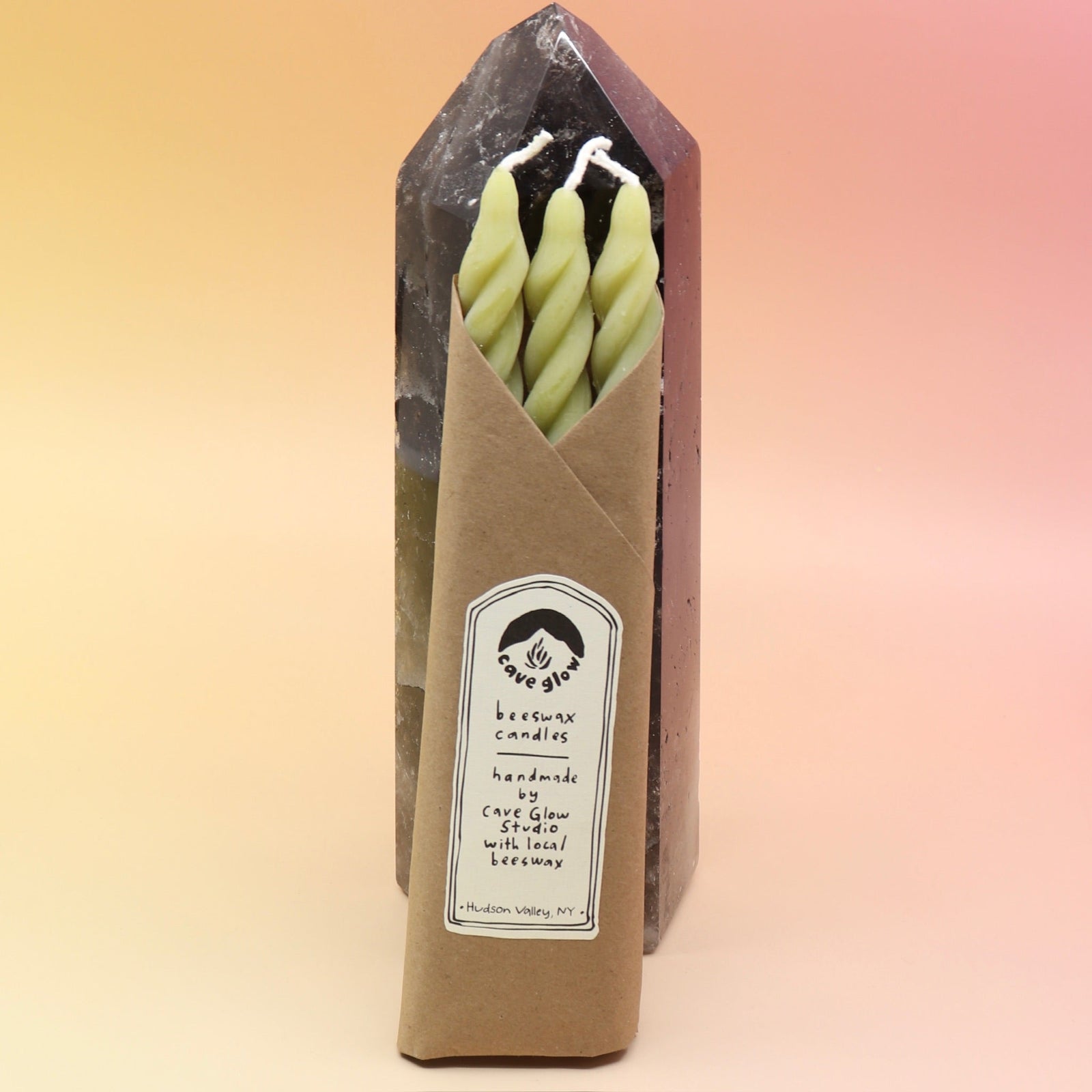 The spiral Chartreuse Beeswax Taper Candles against a crystal tower all on a pink and yellow background.