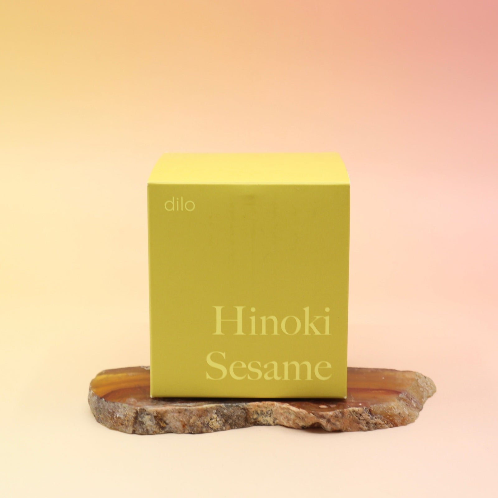 The Hinoki Sesame Candle on an agate slice all on a pink and yellow background.