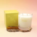 The Hinoki Sesame Candle on an agate slice next to its box all on a pink and yellow background.