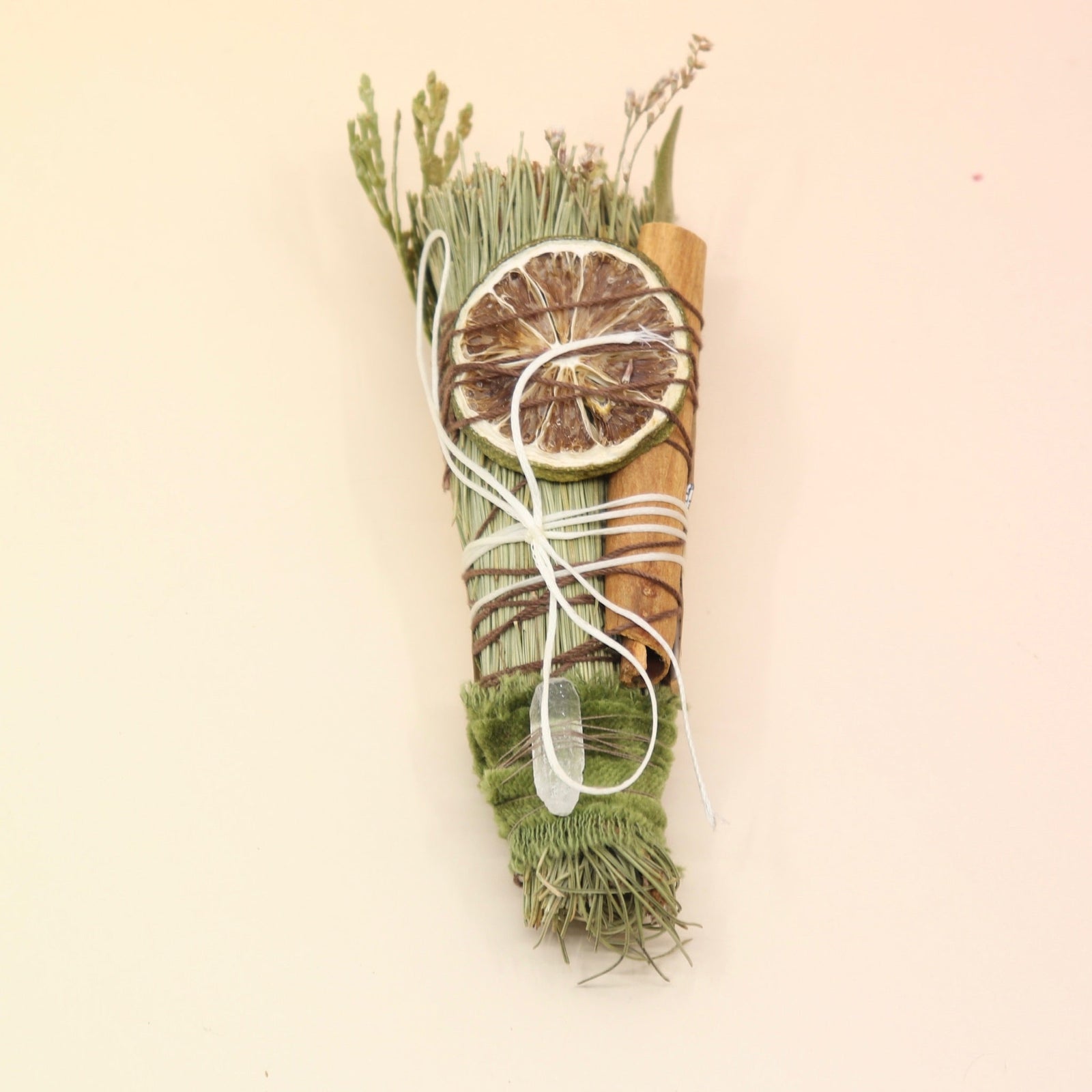 The Piñon Pine Sacred Smoke Cleansing Stick with Quartz Crystal on a pink and yellow background.