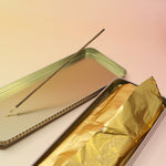 The Premium Incense on a pink and yellow background, showing off the inside of the tin.