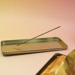 The Premium Incense on a pink and yellow background, showing off the inside of the tin.