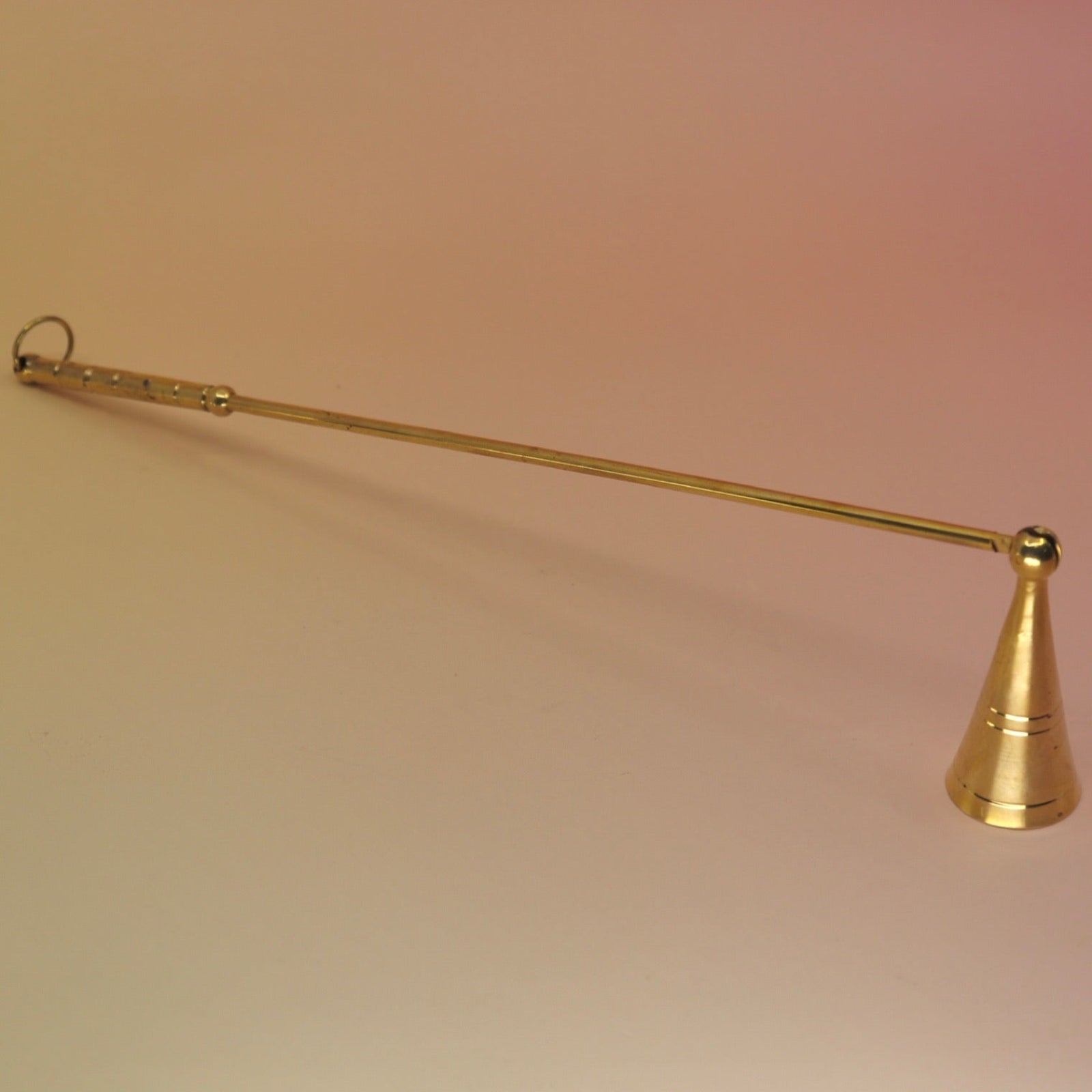 The Brass Candle Snuffer on a pink and yellow background.