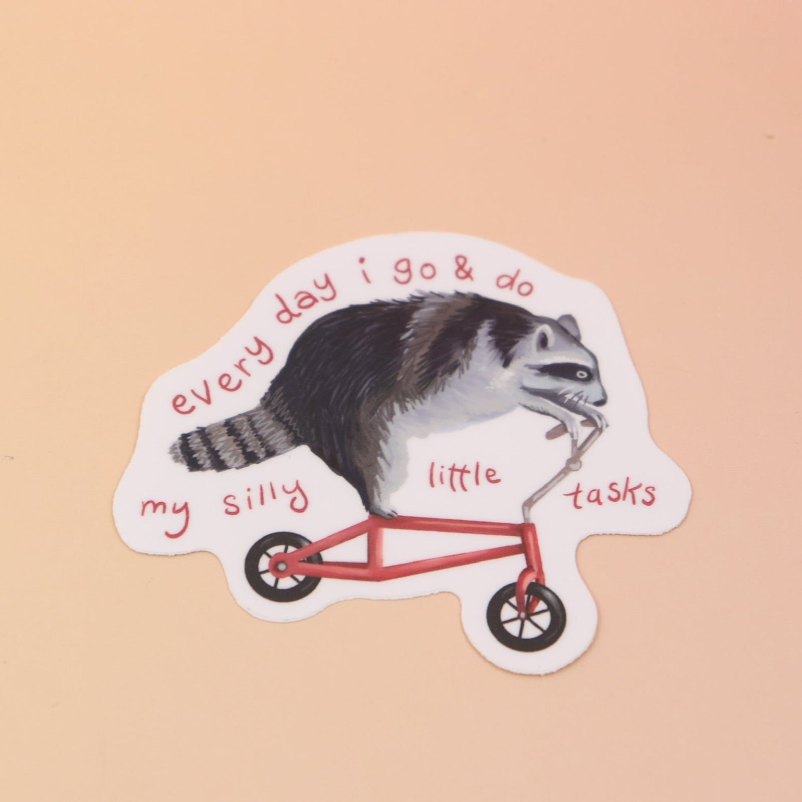 The Raccoon on Bike Vinyl Sticker on a pink and yellow background.
