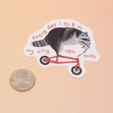 The Raccoon on Bike Vinyl Sticker on a pink and yellow background.