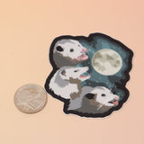 The Three Possum Moon Vinyl Sticker next to a quarter on a pink and yellow background.