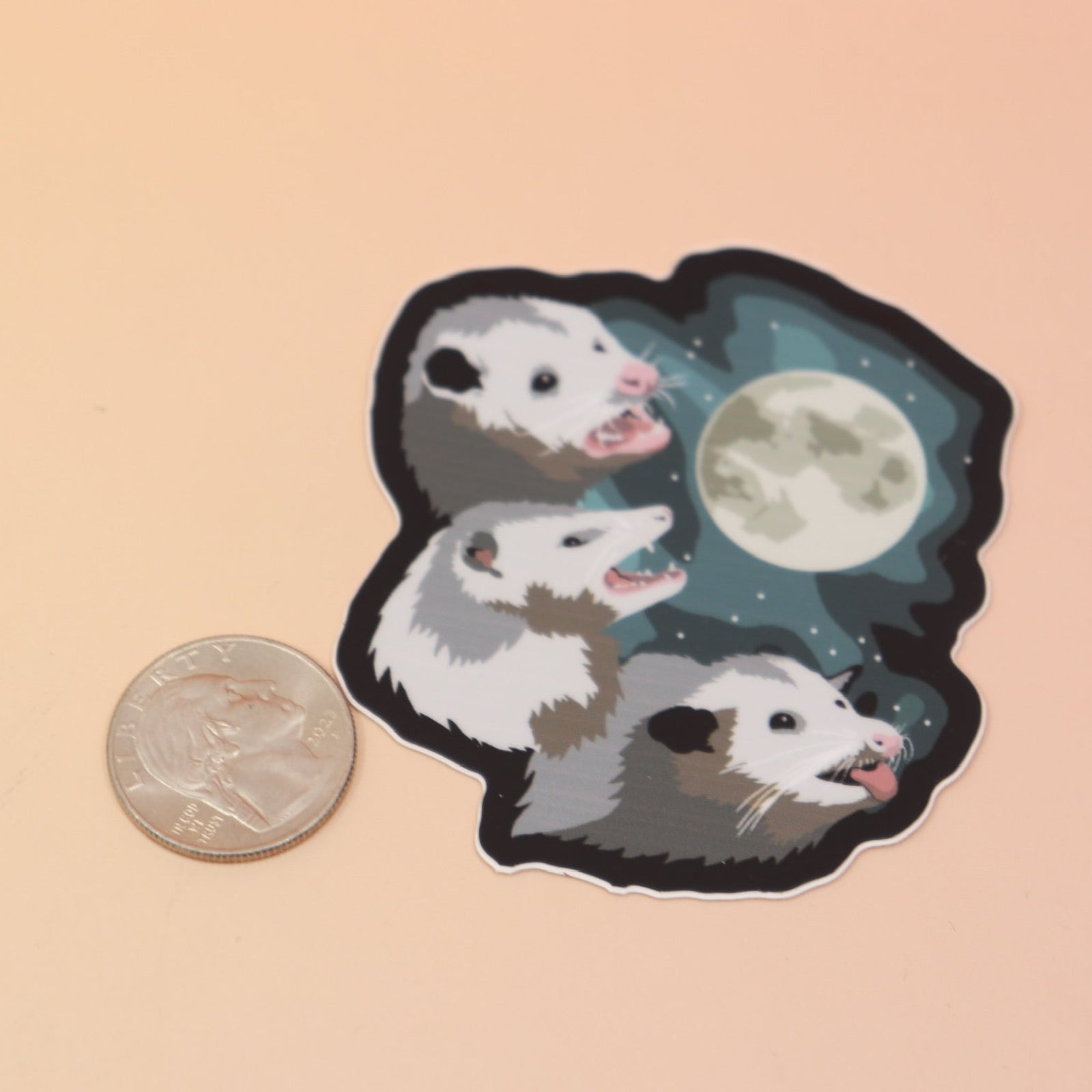 The Three Possum Moon Vinyl Sticker next to a quarter on a pink and yellow background.