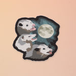 The Three Possum Moon Vinyl Sticker on a pink and yellow background.
