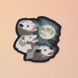 The Three Possum Moon Vinyl Sticker on a pink and yellow background.