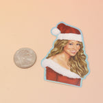 The Mariah Carey Christmas Sticker next to a quarter on a pink and yellow background.
