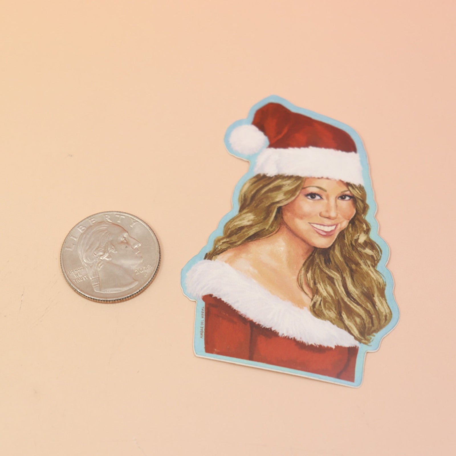 The Mariah Carey Christmas Sticker next to a quarter on a pink and yellow background.