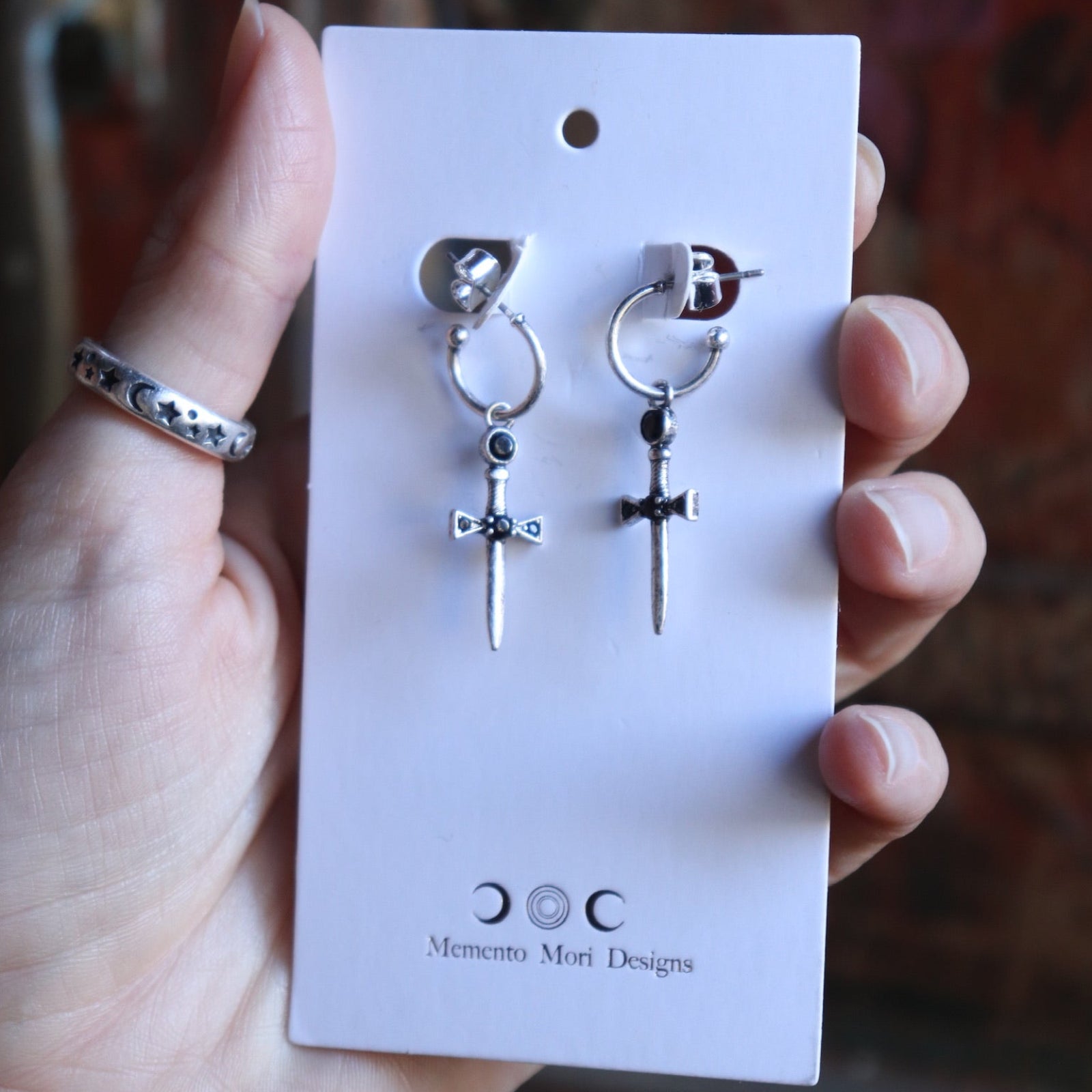Someone holding the Silver Sword Hoop Earrings while they are on their card.