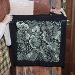 Someone holding up the Black Slime Mold Cotton Bandana in front of a wooden background.
