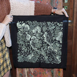 Someone holding up the Black Slime Mold Cotton Bandana in front of a wooden background.