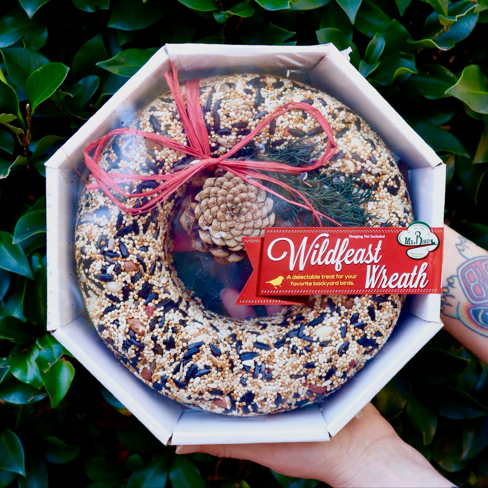 Someone holding the WildFeast Wreath in front of a green bush.
