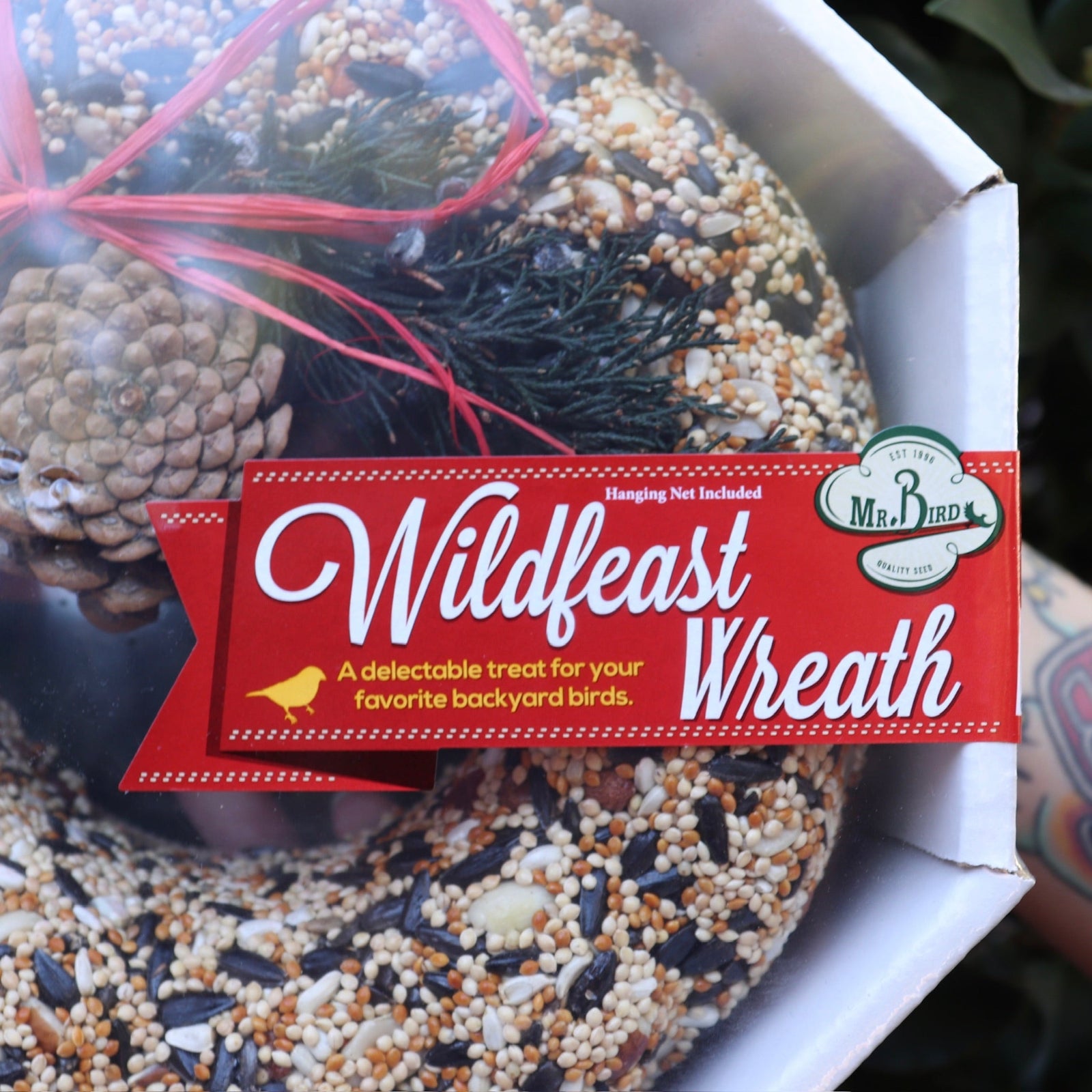 An up-close image of someone holding the WildFeast Wreath in front of a green bush.
