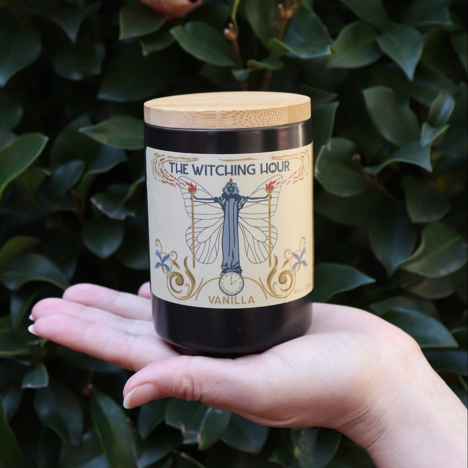 Someone holding the Witching Hour Garden Candle in front of a green bush.