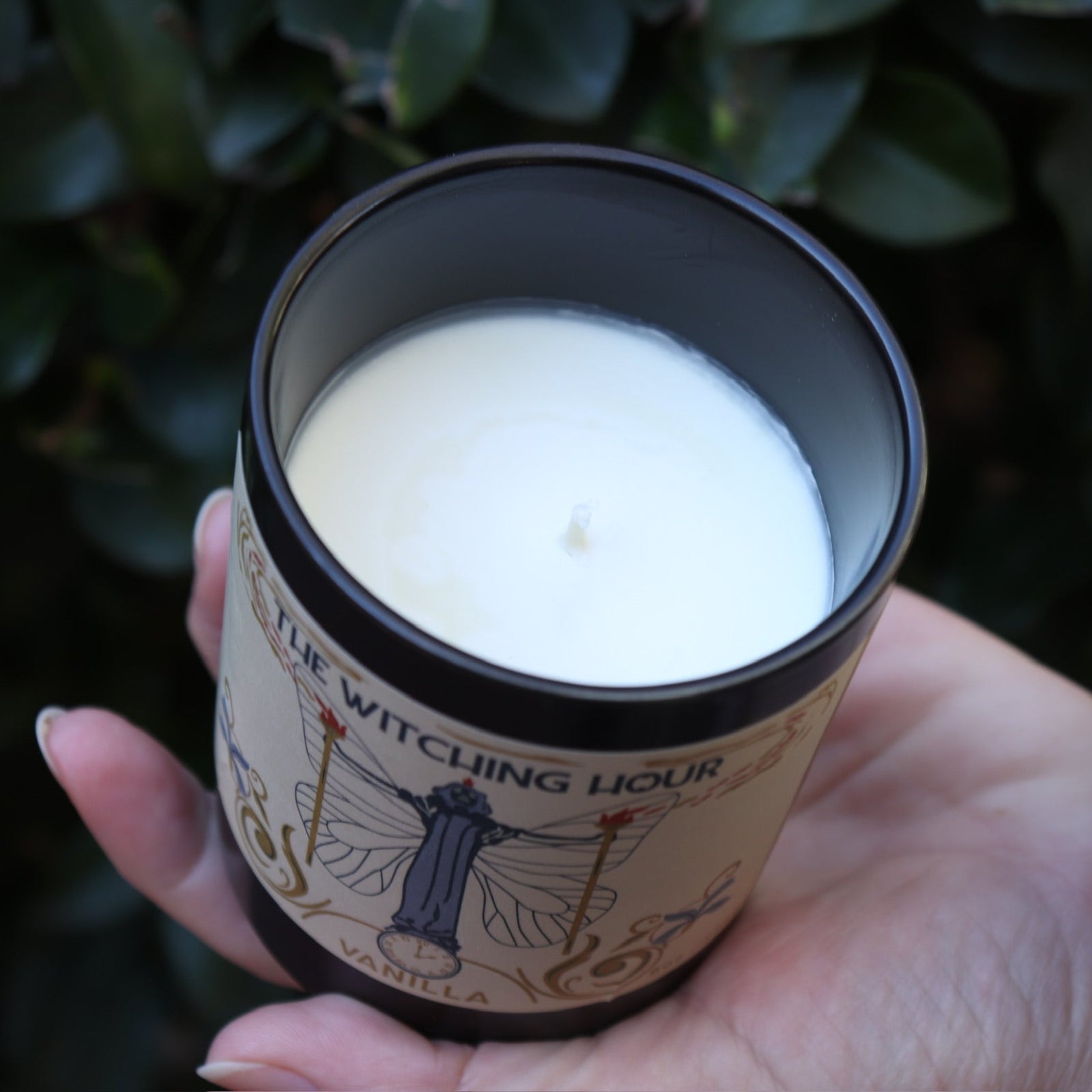 Someone holding the Witching Hour Garden Candle in front of a green bush, showing off the inside.
