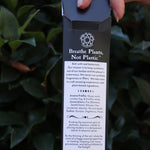 Someone holding the Samhain Premium Incense in front of greenery, showing off the back.