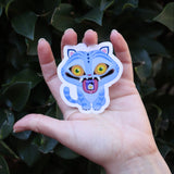 Someone holding the Derpy Tiger Kpop Demon Hunter Inspired Sticker in front of a green bush.