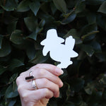 Someone holding the Sussie the Magpie KPop Demon Hunter Inspired Sticker in front of a green bush, showing off the back.