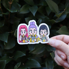 Someone holding the Huntrix Ramen KPop Demon Hunters Inspired Sticker in front of a green bush.