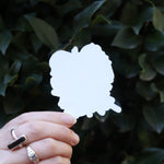 Someone holding the Chibi Saja Boys KPop Demon Hunters Inspired Sticker in front of a green bush, showing off the back.