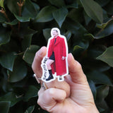 Someone holding the Slutty Little Knee Pedro Pascal Funny Sticker in front of a green bush.