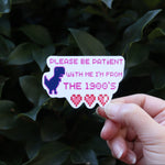 Someone holding the Please Be Patient With Me Millennial Funny Sticker in front of a green bush.