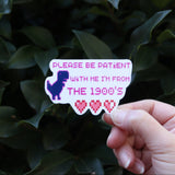 Someone holding the Please Be Patient With Me Millennial Funny Sticker in front of a green bush.