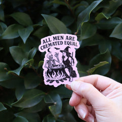 Someone holding the Feminist Halloween Sticker in front of a green bush.