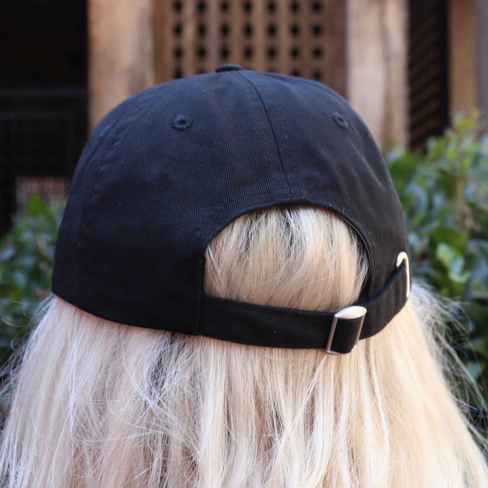 A woman wearing the Actual Ghost Black Unisex Baseball Cap in front of a green bush, showing off the back.