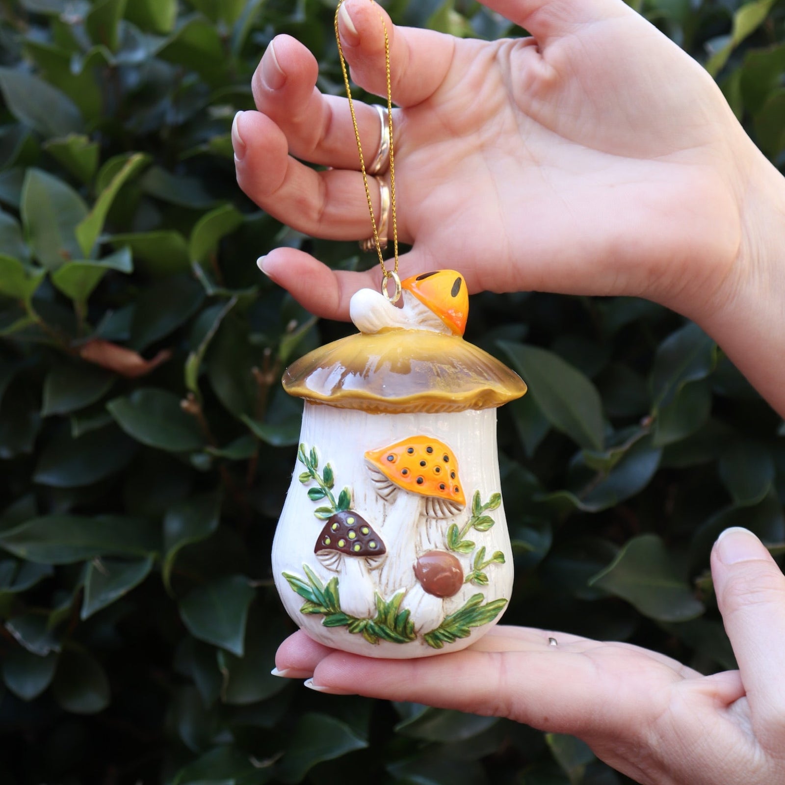 Someone holding the Merry Mushroom 70s Inspired Hand-Painted Retro Ornament in front of a green bush.
