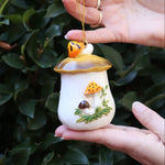 Someone holding the Merry Mushroom 70s Inspired Hand-Painted Retro Ornament in front of a green bush, showing off the side.