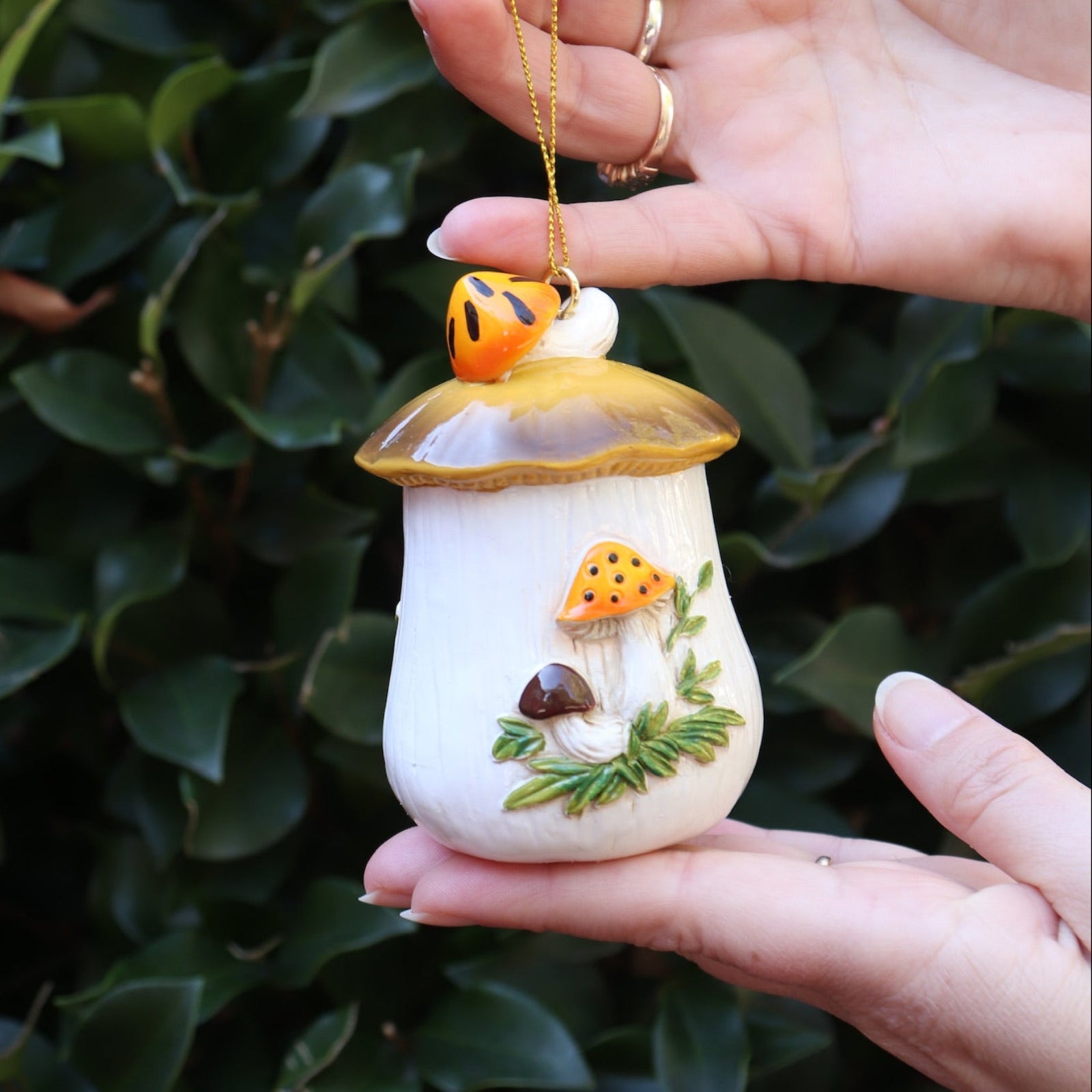Someone holding the Merry Mushroom 70s Inspired Hand-Painted Retro Ornament in front of a green bush, showing off the side.