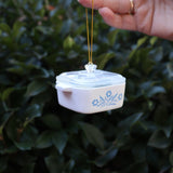 Someone holding the Mini Cornflower Casserole Ornament in front of a green bush.