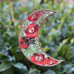 Someone holding the Moon Roses Witchy Christmas Ornament in front of a green bush.